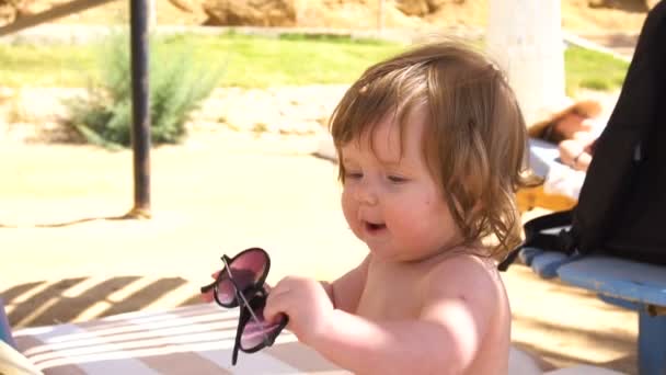 Niña sentada con gafas de sol en las manos — Vídeo de stock