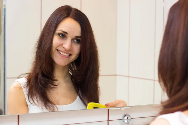 Mujer joven cepillándose el pelo en el baño — Foto de Stock