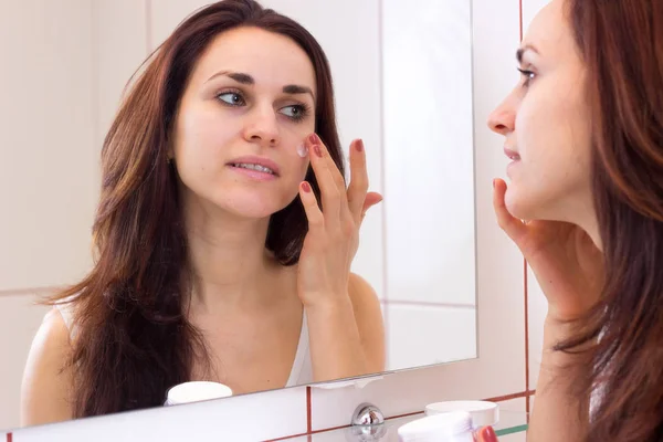 Молода жінка використовує крем для обличчя у ванній — стокове фото