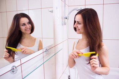 Genç bir kadın banyoda saçını tarıyor.