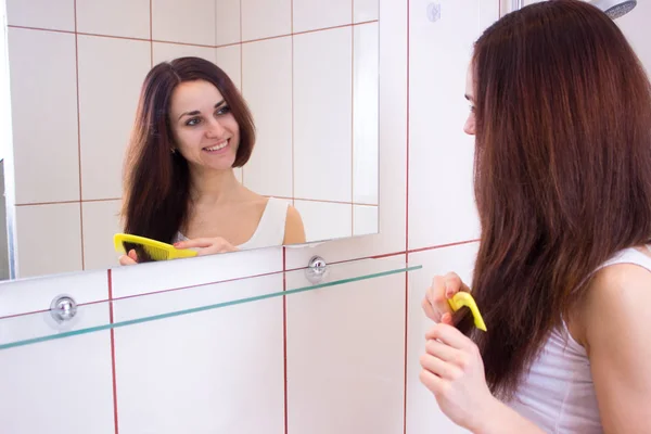 Mujer joven cepillándose el pelo en el baño —  Fotos de Stock