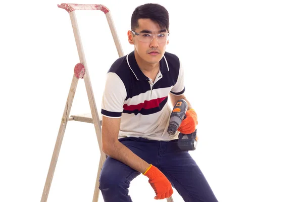 Young man holding electric screwdriver and sitting on ledder — Stock Photo, Image