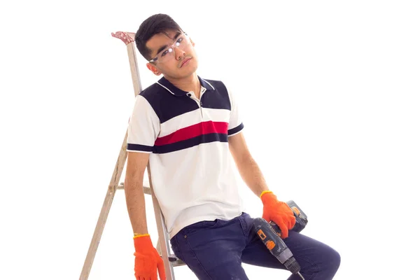 Young man holding electric screwdriver and sitting on ledder — Stock Photo, Image