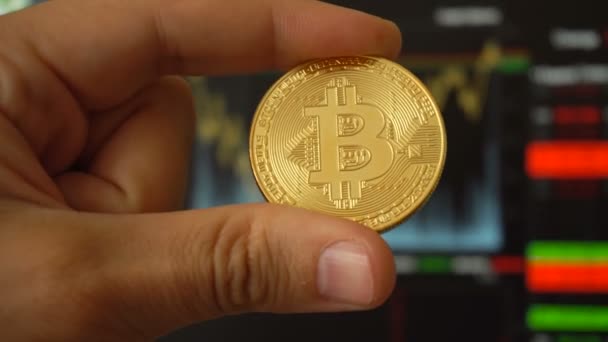 Bitcoin digitale Münze in den Händen von Mann gegenüber Handelsterminal — Stockvideo