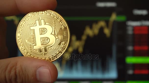 Bitcoin-Münze in Händen eines Mannes gegenüber Handelsterminal — Stockvideo