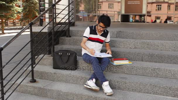 亚洲男同学坐在楼梯上，阅读本书 — 图库视频影像