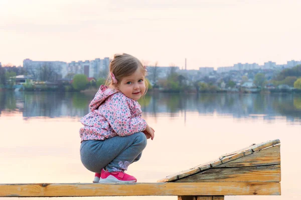 Kleines Mädchen träumt davon, auf der Bank in der Nähe des Flusses zu sitzen — Stockfoto