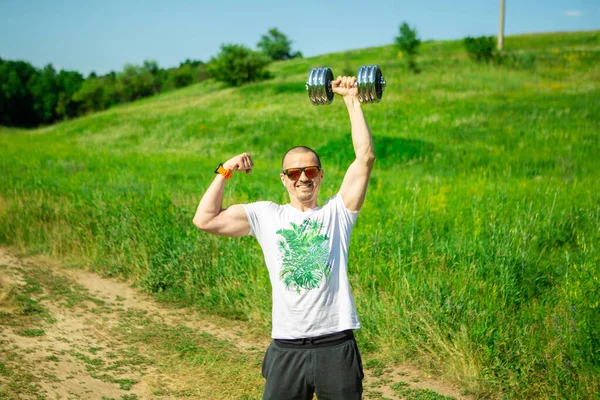 Przystojny mężczyzna z hantlami w jednej ręce pokaż bicepsy — Zdjęcie stockowe