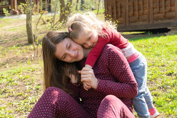 Маленькая девочка обнимает женщину, которая сидит на траве — стоковое фото