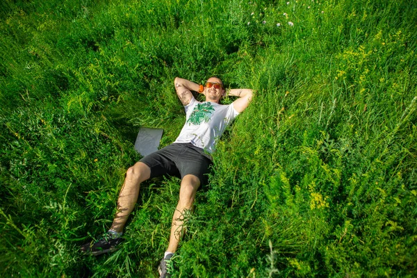 Man lying down on grass with laptop. Top view