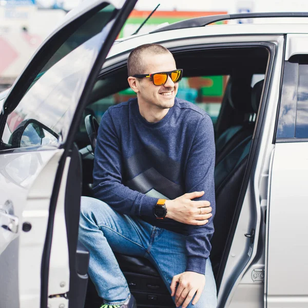 Dorosły mężczyzna w czerwonych okularach siedzi w samochodzie z otwartymi drzwiami — Zdjęcie stockowe