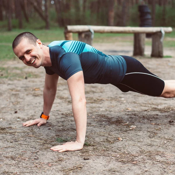 Atletický muž se usmívá, zatímco dělá kliky venku — Stock fotografie