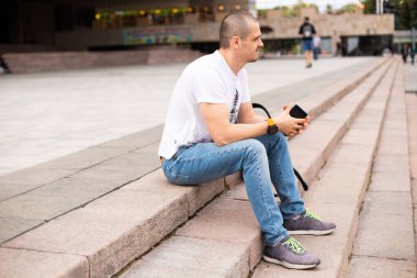 Beyaz tişörtlü ve kot pantolonlu bir adam merdivenlerde oturuyor.