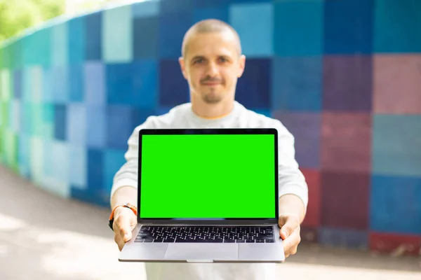 Muž se dívá do kamery a drží notebook se zelenou chroma klávesnicí — Stock fotografie