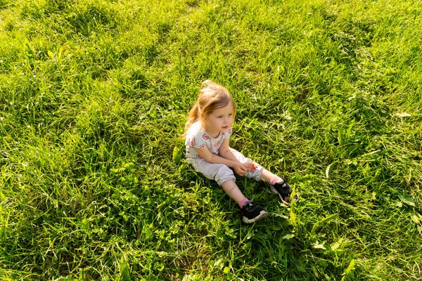 Маленькая девочка сидит на лужайке в летний солнечный день — стоковое фото