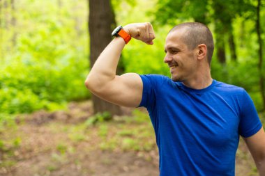 Gülümseyen sporcu pazılarını açık havada gösteriyor.