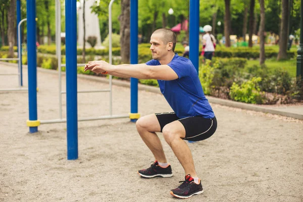 Hombre haciendo sentadillas en el campo de deportes en el parque —  Fotos de Stock