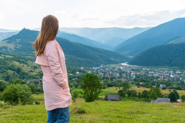 Frau steht auf einem Gipfel und blickt auf Tal mit Dorf und Bergen — Stockfoto