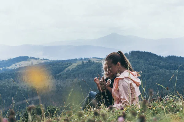 Мать и дочь сидят на холме с видом на горы позади — стоковое фото