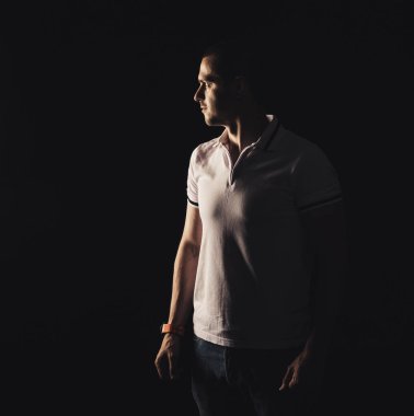 Yetişkin bir adam siyah arka plana bakıyor.