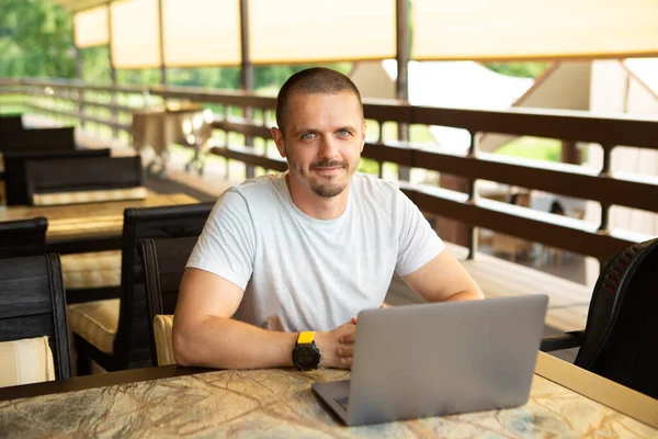 Glimlachende man zit aan het bureau in restaurant met laptop en werkt online — Stockfoto