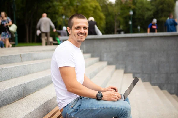 Man freelancer met laptop zittend in stedelijk park — Stockfoto