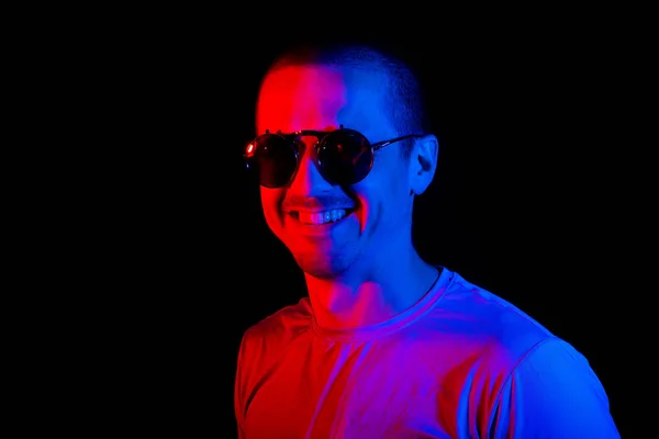 Man ler och tittar i kameran i solglasögon med färg blått och rött ljus — Stockfoto