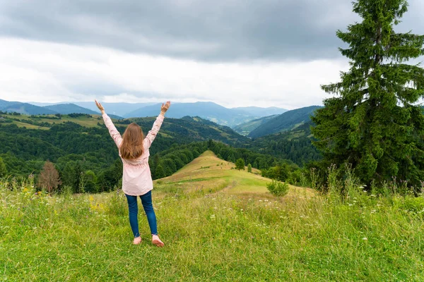 Glückliche Frau steht auf grünem Hügel und blickt auf Berge — Stockfoto