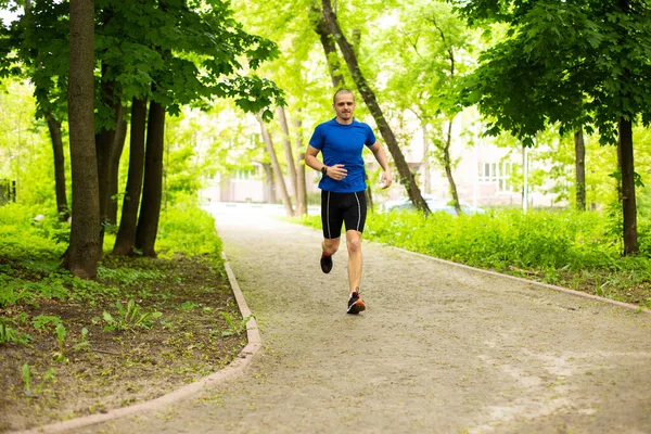 Muž v modrém tričku běží v lese nebo parku — Stock fotografie