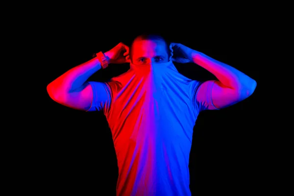 Ο άνθρωπος κρύβει το πρόσωπό του κάτω από το t-shirt, κόκκινο και μπλε φως χρώμα — Φωτογραφία Αρχείου