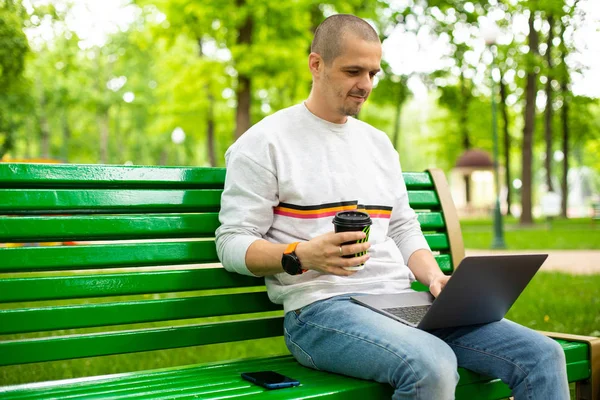Hombre sosteniendo la taza de café y trabajando en el ordenador portátil —  Fotos de Stock