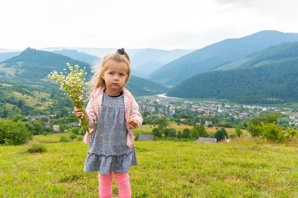 Egy kislány, aki a kamerába néz, és virágokat tart a kezében. — Stock Fotó