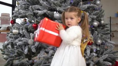 Little girl shaking red gift box and trying to understand what inside