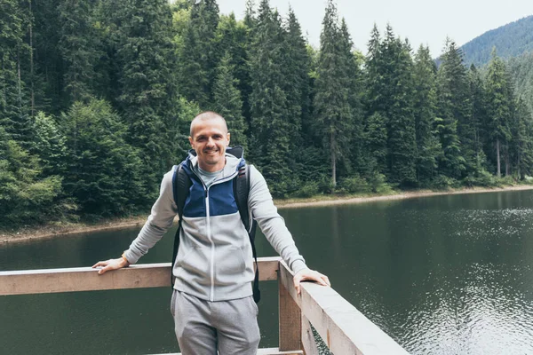 Homme souriant et regardant à la caméra avec lac de montagne et forêt derrière — Photo