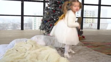 Sevimli küçük kız arkasında Noel ağacı ile yatakta zıplıyor.