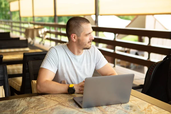 Man freelancer looking away sitting on desk in cafe with laptop