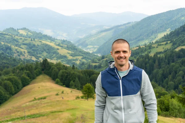 Uomo sorridente guardando in macchina fotografica con vista sulle montagne dietro — Foto Stock