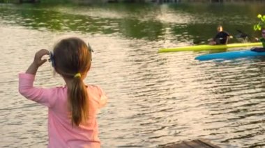 Küçük kız iki adamın nehirde kano yapmasını seyrediyor.