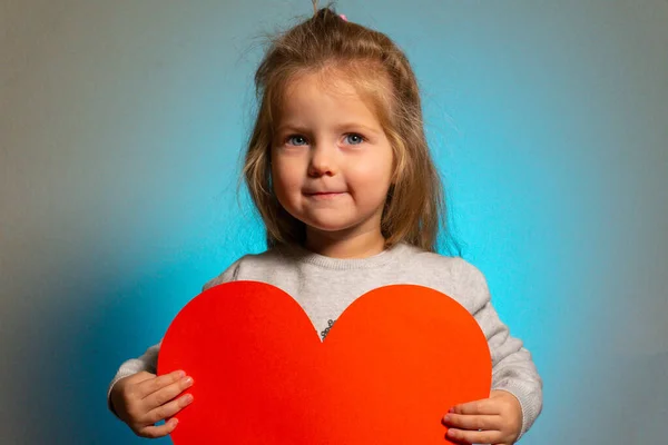 Malá dívka s červeným velkým prázdným srdcem dívá do kamery — Stock fotografie