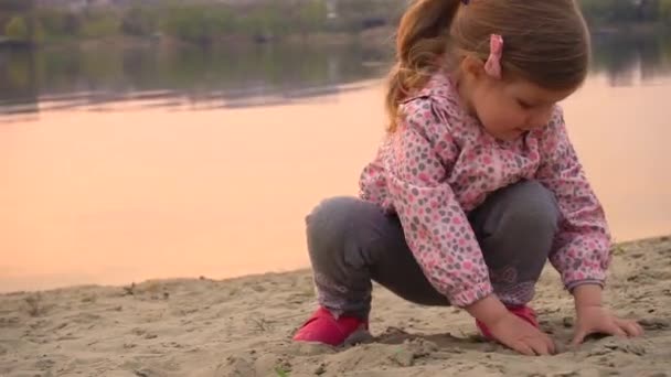 Child girl playing in sand on beach near river or lake — Stockvideo