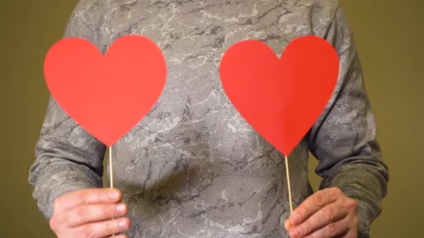 Mężczyzna trzyma dwa czerwone papierowe serca na patykach — Wideo stockowe