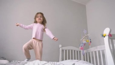 Küçük tatlı kız yatakta zıplıyor ve eğleniyor.