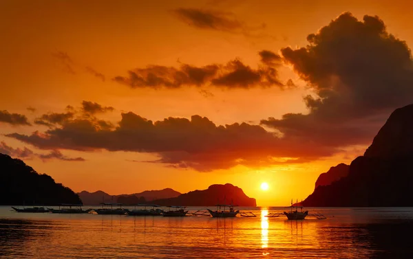 Barcos filippino tradicionales en la bahía de El Nido con luces de puesta de sol . Imagen De Stock