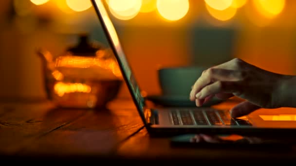 Dedos femeninos escribiendo en el ordenador portátil en semidark ajuste cálido. Fondo bokeh redondo amarillo brillante. Disparo deslizante, 4K — Vídeos de Stock