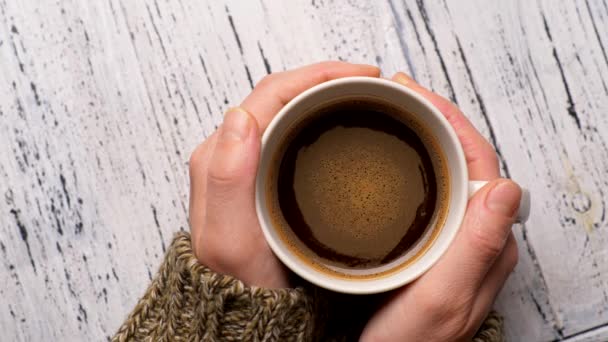 Vrouwelijke handen die een kop koffie vasthouden. Schuimige bruine en oranje vloeistof drank roteren in witte beker. Bovenste schot, 4k. — Stockvideo