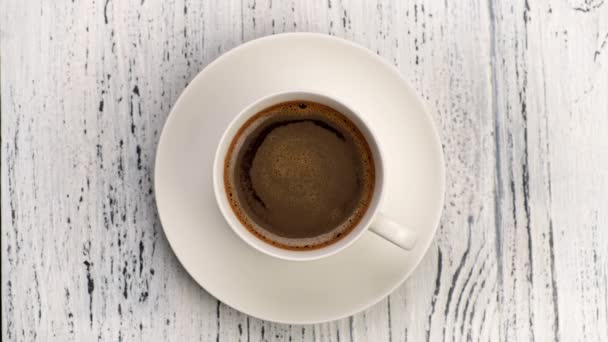 Top down shot of coffee foam swirls in white cup with coffee. Old wooden background, 4K — Stock Video