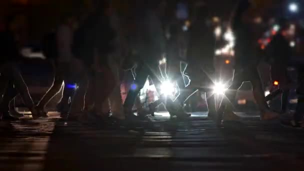Multidão irreconhecível de pessoas atravessando um pedestre na frente de carros parados iluminação com faróis durante a hora de ponta da noite. Lento tiro em movimento, UHD — Vídeo de Stock
