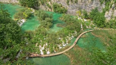 Hırvatistan 'ın Plitvice Gölleri Ulusal Parkı' ndaki şelaleler ve şelaleler, yeşil flora ve turkuaz gölleri arasında yürüyen turistler. Uhd