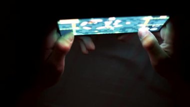 Karanlıkta akıllı telefonuyla oyun oynayan bir çocuk. Koyu arkaplan üzerinde çocuk ve akıllı telefon elleri
