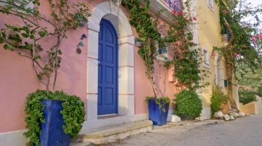 Kefalonia, Yunanistan. Pastel rengi pembe, krem rengi duvarları ve yeşil flora ile süslenmiş mavi kapıları olan bir ev. Turna atışı, 4k.